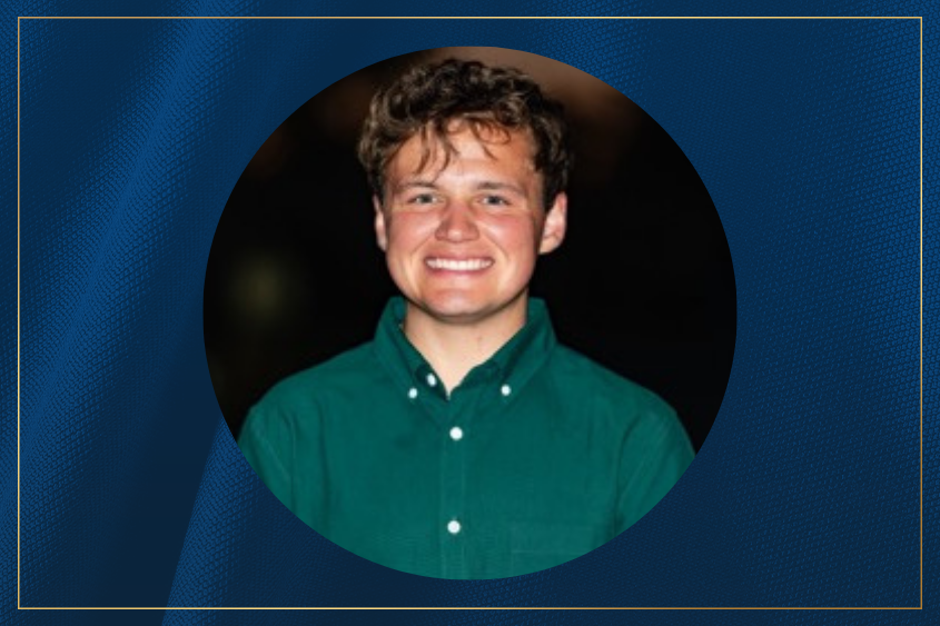 A person smiling and wearing a green button-up shirt stands against a dark background.