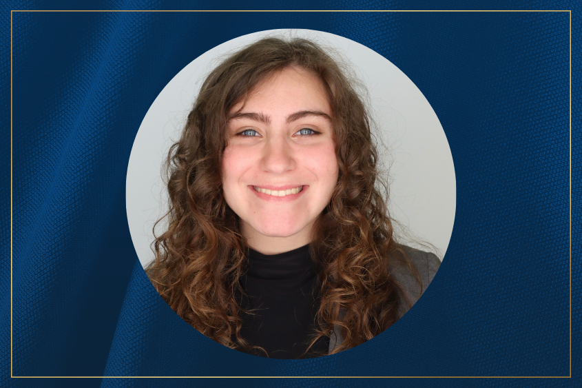 A person with long curly brown hair smiles for the camera wearing a black top.