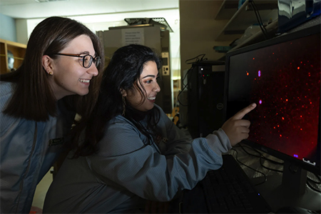 two people in lab gear point at red screen