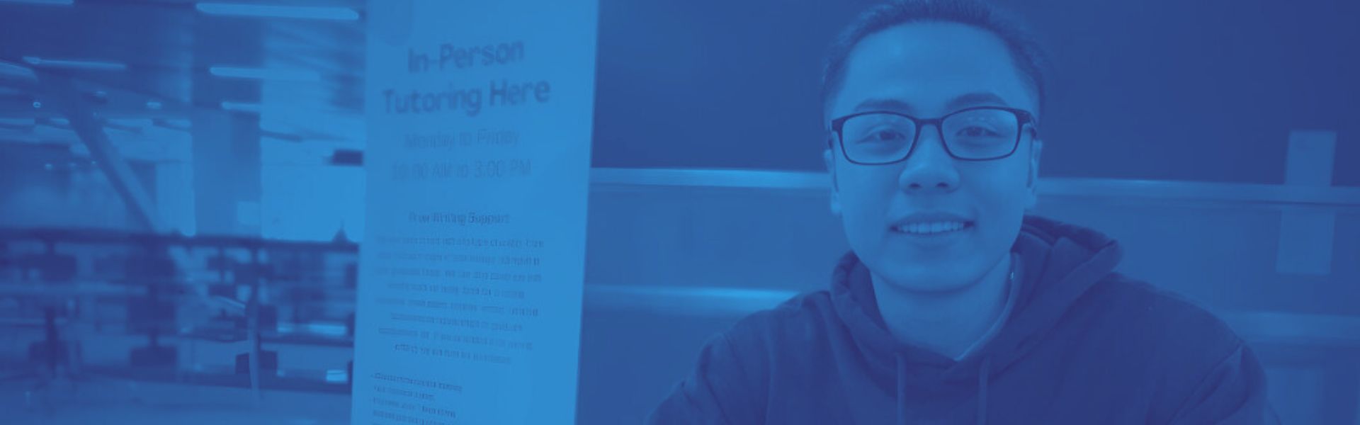 ​Writing tutor seated at rtable by banner with blue color overlay